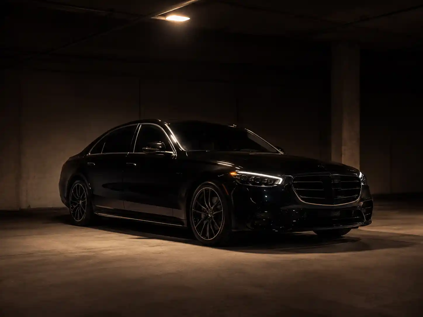 Black luxury sedan with its headlights on, parked in a dimly lit garage