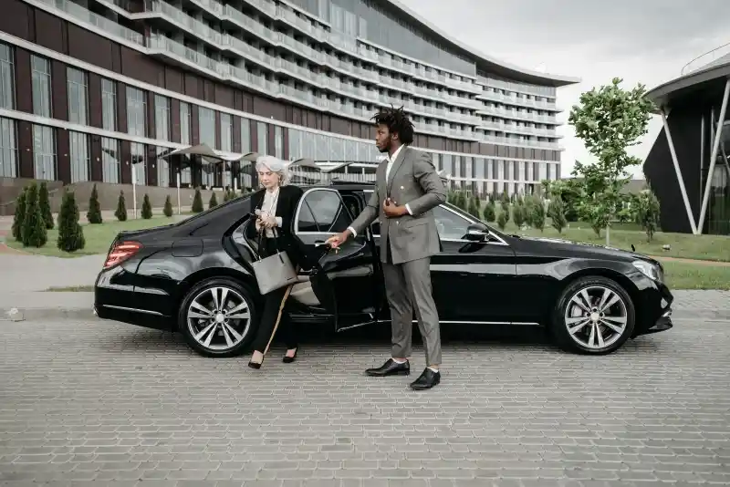 Chauffeur holding the car door as a passenger steps out of a black sedan outside a modern building