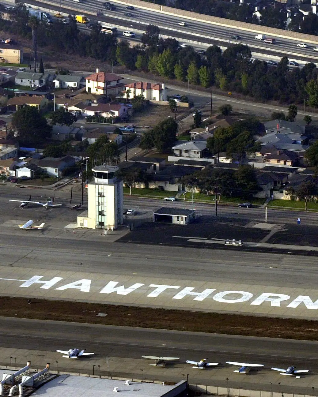 Aerial view of Hawthorne Airport's runway and control tower, with small planes parked along the apron