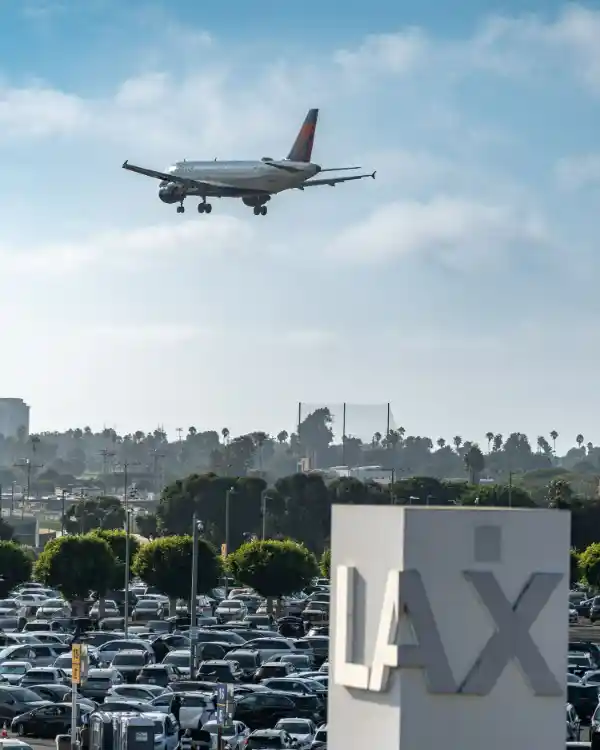 Plane landing over the LAX parking area, with the LAX sign in the foreground
